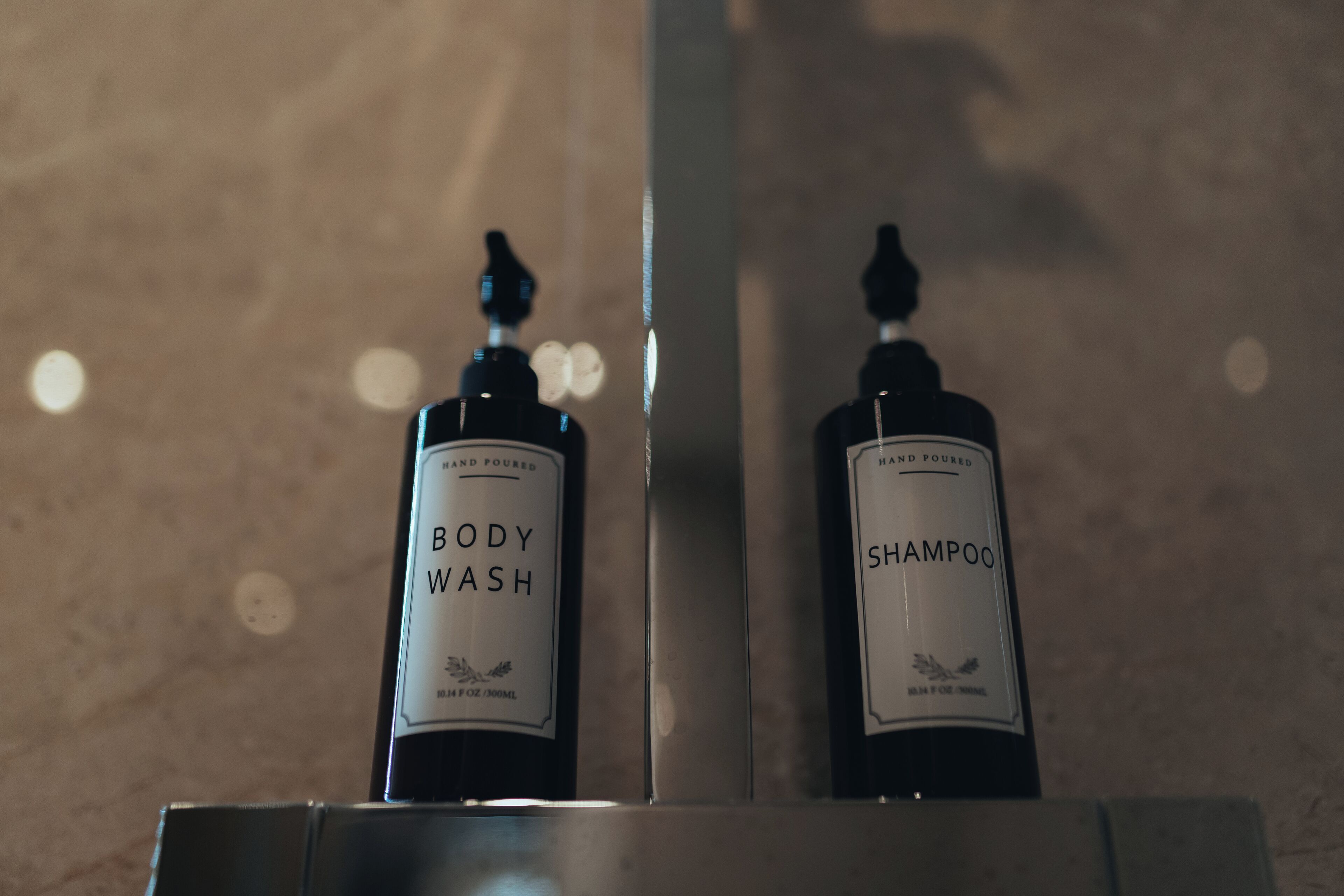Two bottles of body wash and shampoo on a reflective surface.