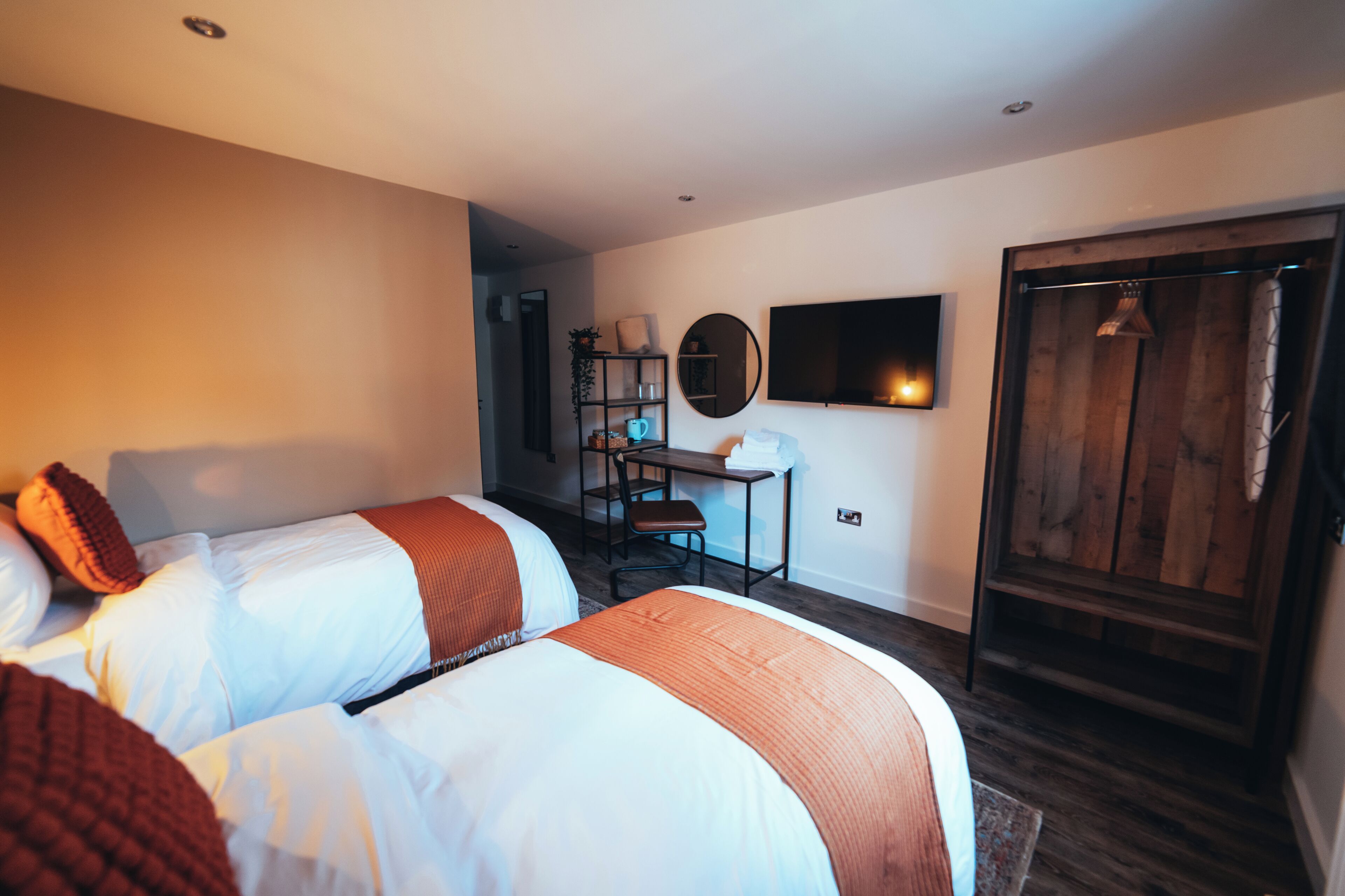 A hotel room with two beds, a desk, a chair, a TV, and a wardrobe.