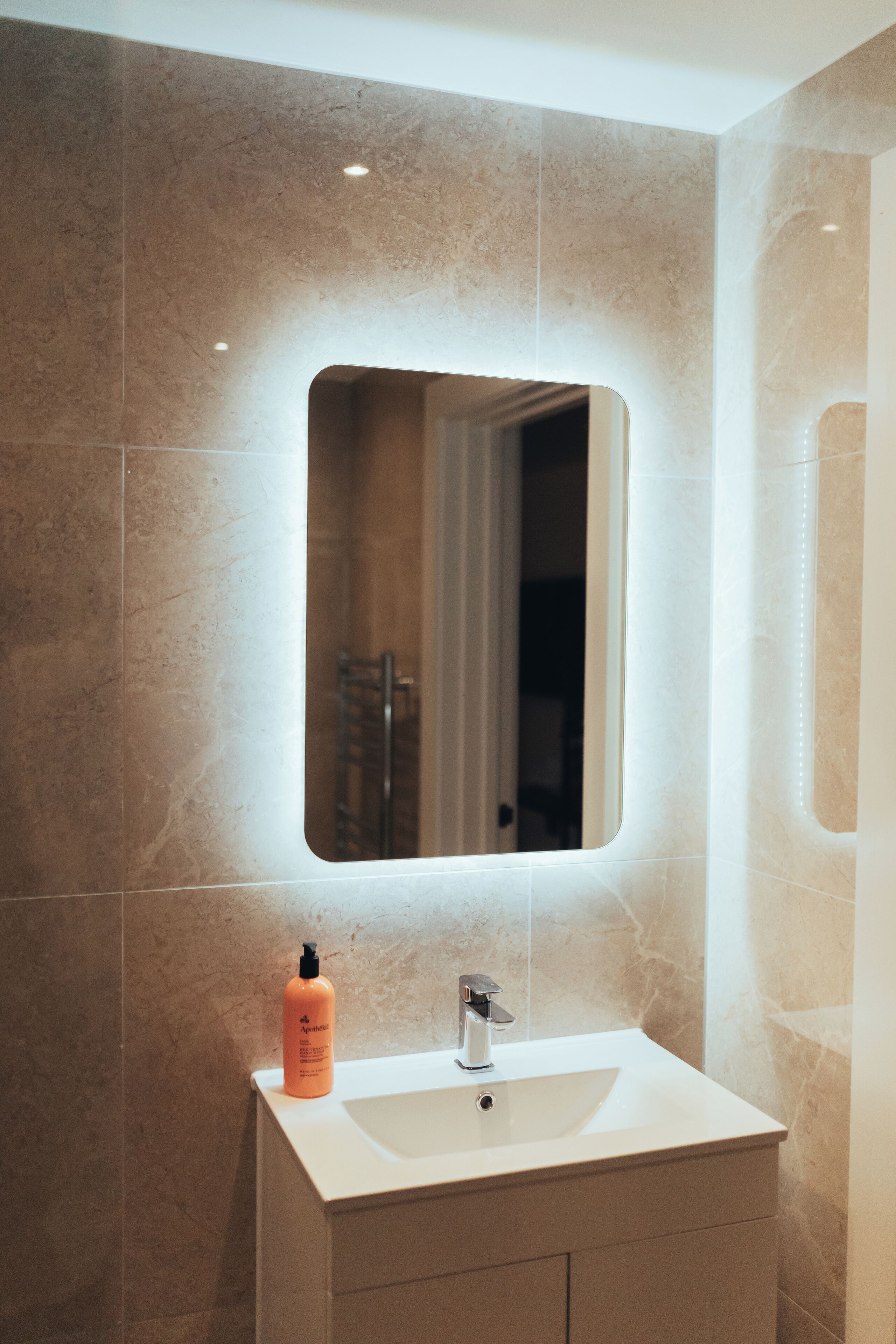 A bathroom with a white sink, a mirror, and a bottle of shampoo.