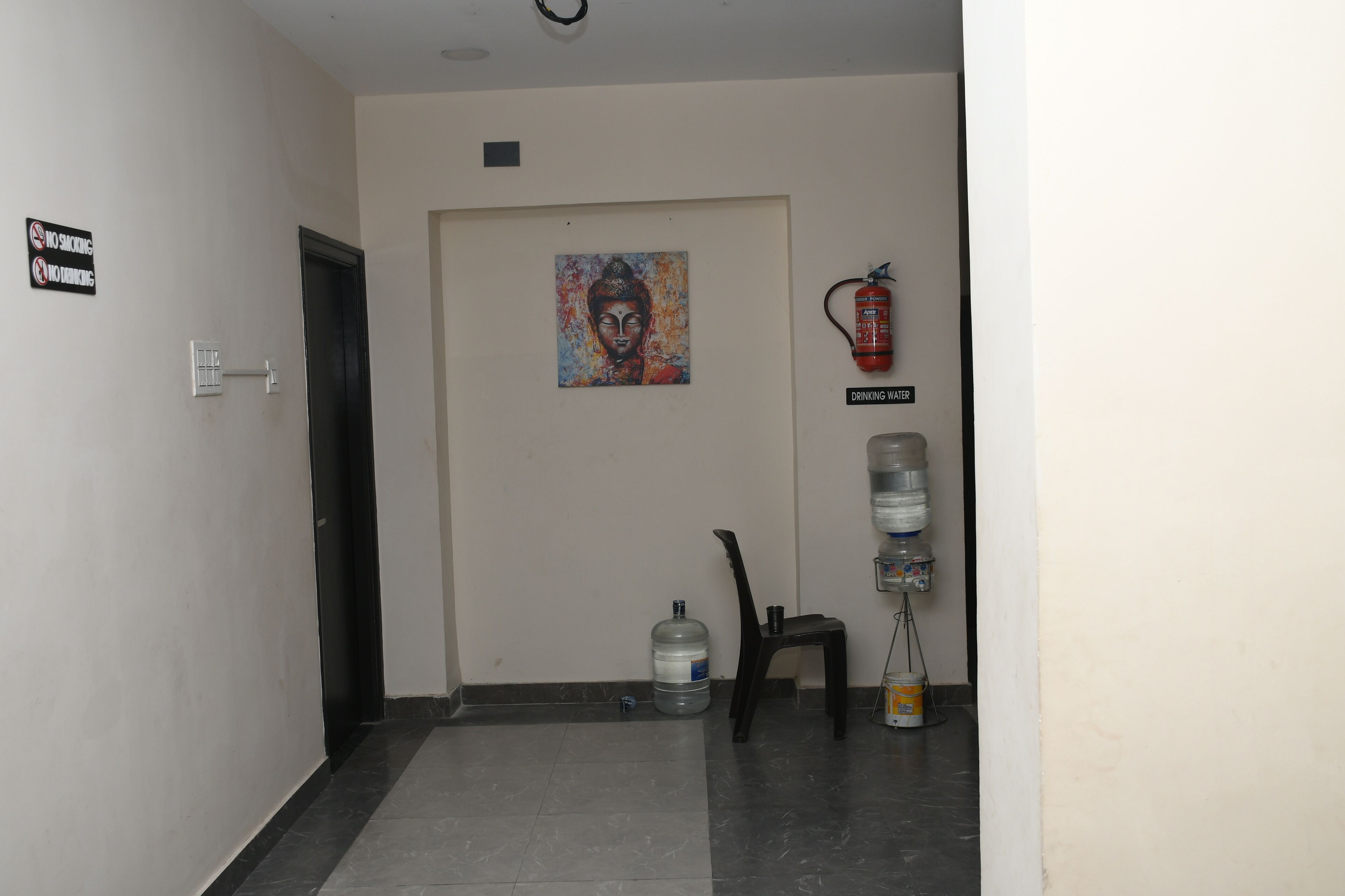A hallway with a no-smoking sign, a Buddha painting, a fire extinguisher, and a water dispenser.