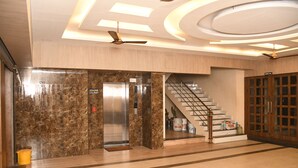 Een moderne lobby met een marmeren muur, een lift, een trap en een houten deur met de tekst 