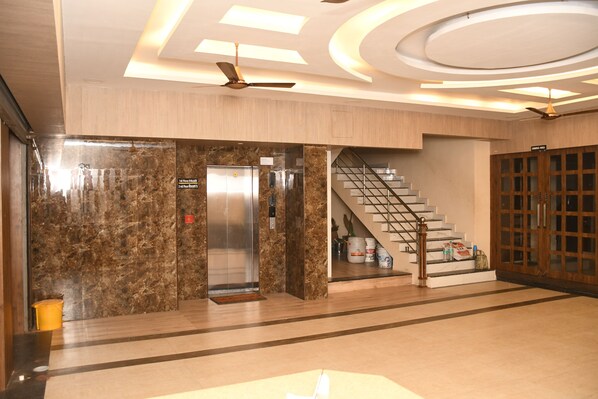 A modern lobby with a marble wall, an elevator, a staircase, and a wooden door labeled "Dining Hall".