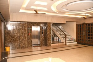 A modern lobby with a marble wall, an elevator, a staircase, and a wooden door labeled "Dining Hall".