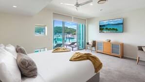 A modern hotel room with a large bed, a ceiling fan, a view of a pool and mountains, and a TV on the wall.