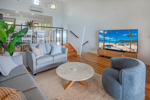 Una sala de estar moderna con un sofá gris, una mesa de centro redonda y un televisor que muestra una escena de playa.