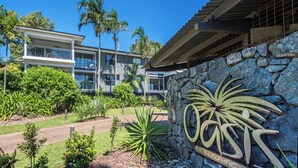 A modern building with a stone wall and a sign that reads "Coast in Hamilton Two." - Oasis 21, Oasis 21 on Hamilton island (Hamilton Island)