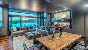 A modern living room with a wooden dining table, leather chairs, and a large window overlooking a scenic lake. - Yacht Club Villa 29, Yacht Club Villa 29 on Hamilton Island (Hamilton Island)