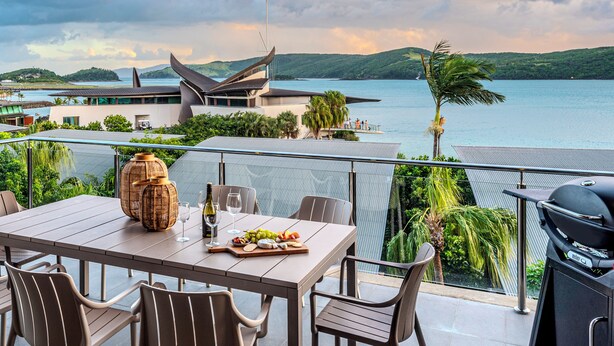 A dining area with a table set for two, overlooking a body of water and a modern building. - Yacht Club Villa 29, Yacht Club Villa 29 on Hamilton Island (Hamilton Island)