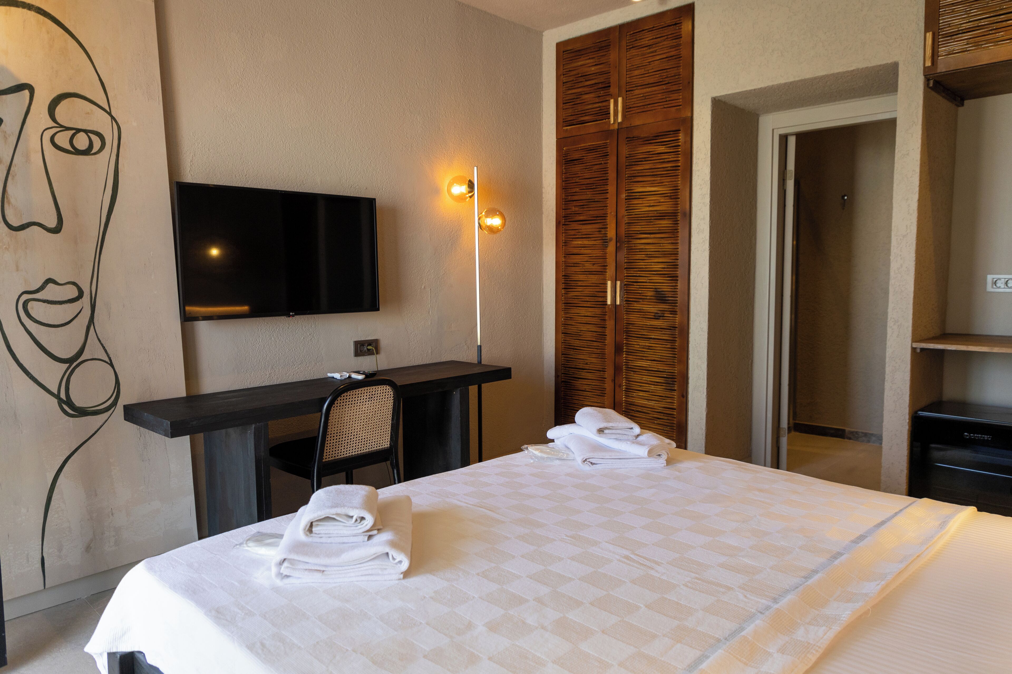A hotel room with a bed, a desk, a chair, a TV, and a wardrobe.