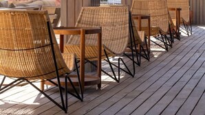 A wooden deck with wicker chairs and tables, overlooking a scenic area with trees and a building in the background. - SEA SOUL OTEL (Bodrum)