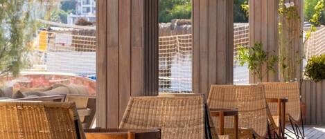 A wooden deck with wicker chairs and tables, overlooking a scenic area with trees and a building in the background.
