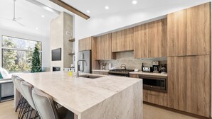 Una cucina moderna con un'isola grande, mobili in legno, elettrodomestici in acciaio inossidabile e un'ampia finestra vista alberi.