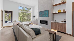 Un soggiorno moderno con un divano beige, un caminetto e un angolo cottura con mobili in legno e un piano di lavoro.