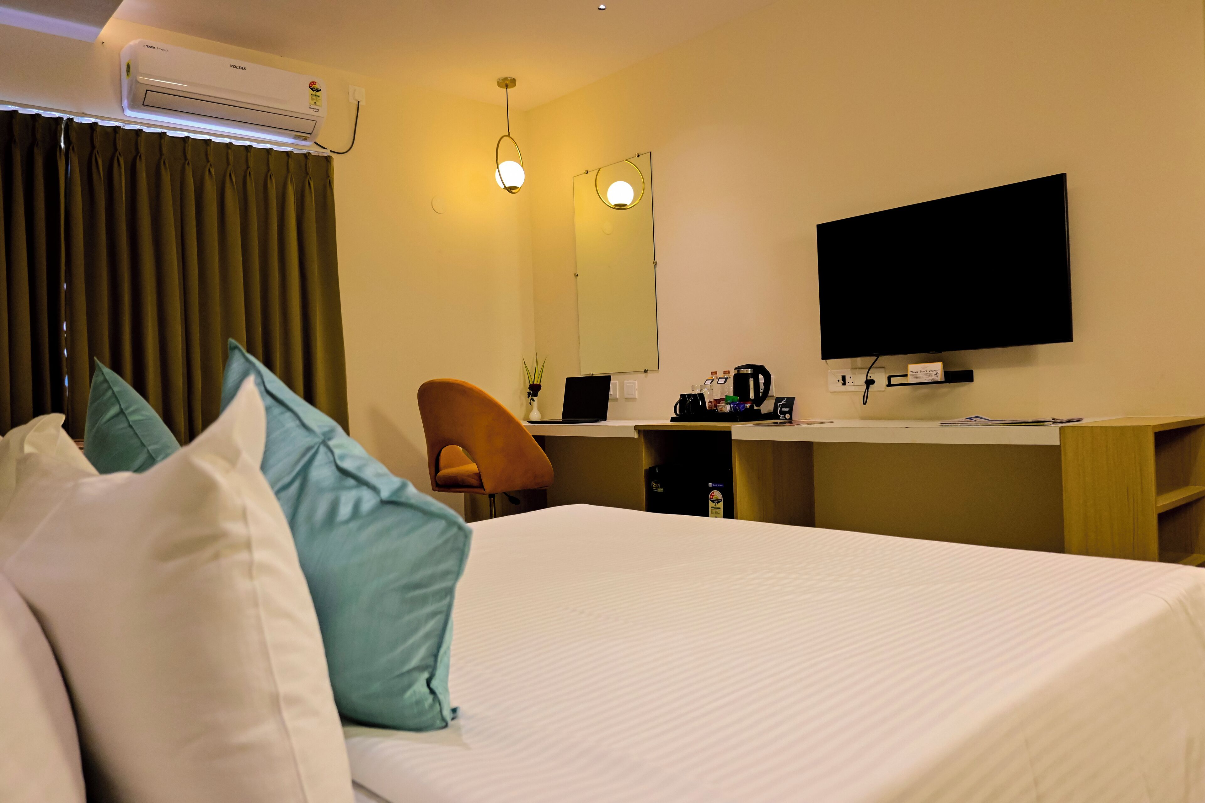 Una habitación de hotel con cama, escritorio, silla, televisión y aire acondicionado.