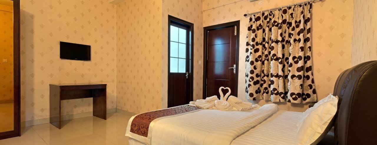 Une chambre d’hôtel avec un lit, un téléviseur fixé au mur, une table de chevet et une porte avec une fenêtre.
