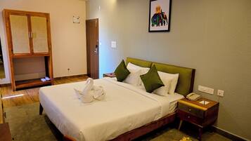 A neatly arranged hotel room with a large bed, a wooden wardrobe, a bedside table with a lamp, and a small table with fruit.