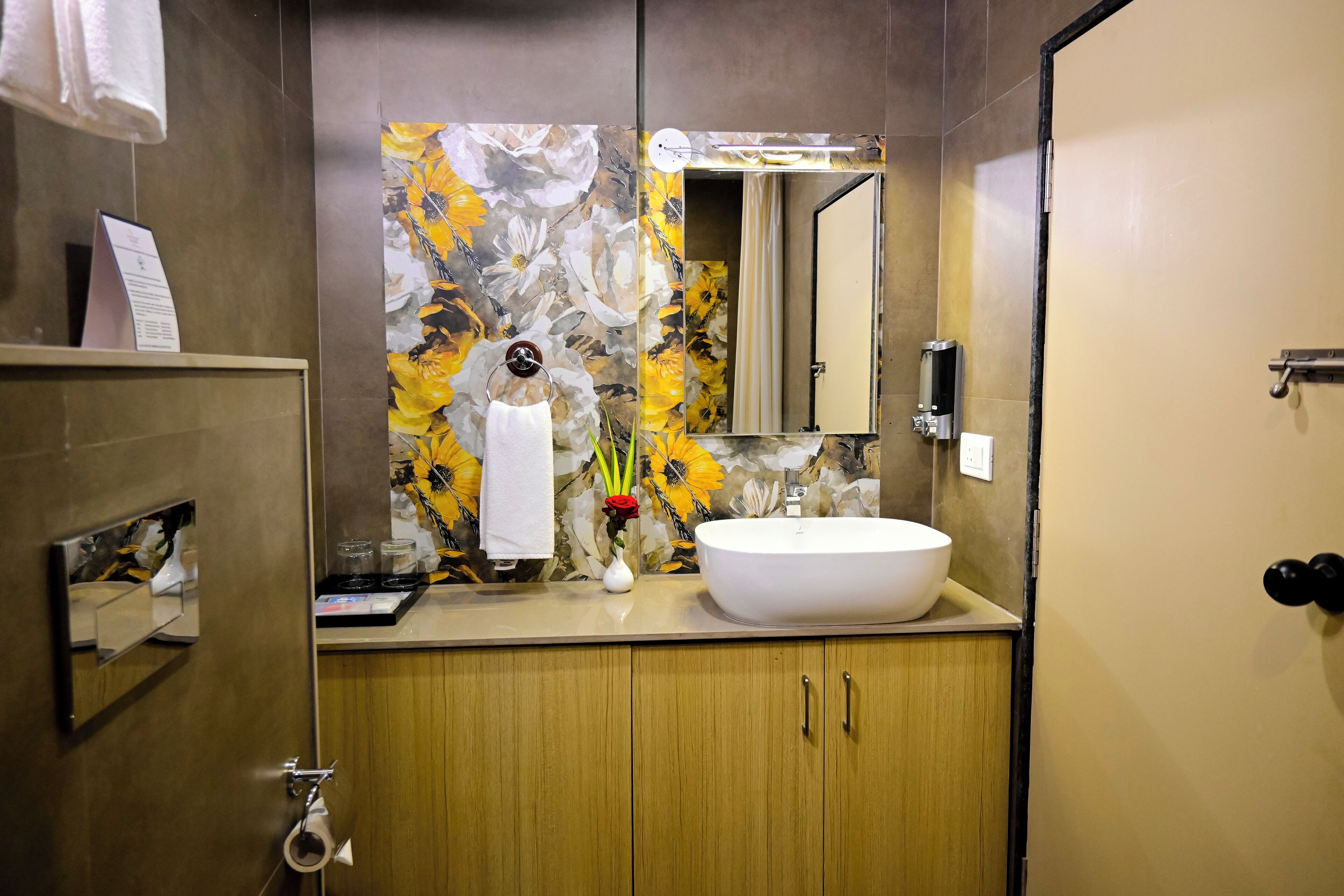 A modern bathroom with a large sink, wooden cabinets, a mirror, and a floral wall design.