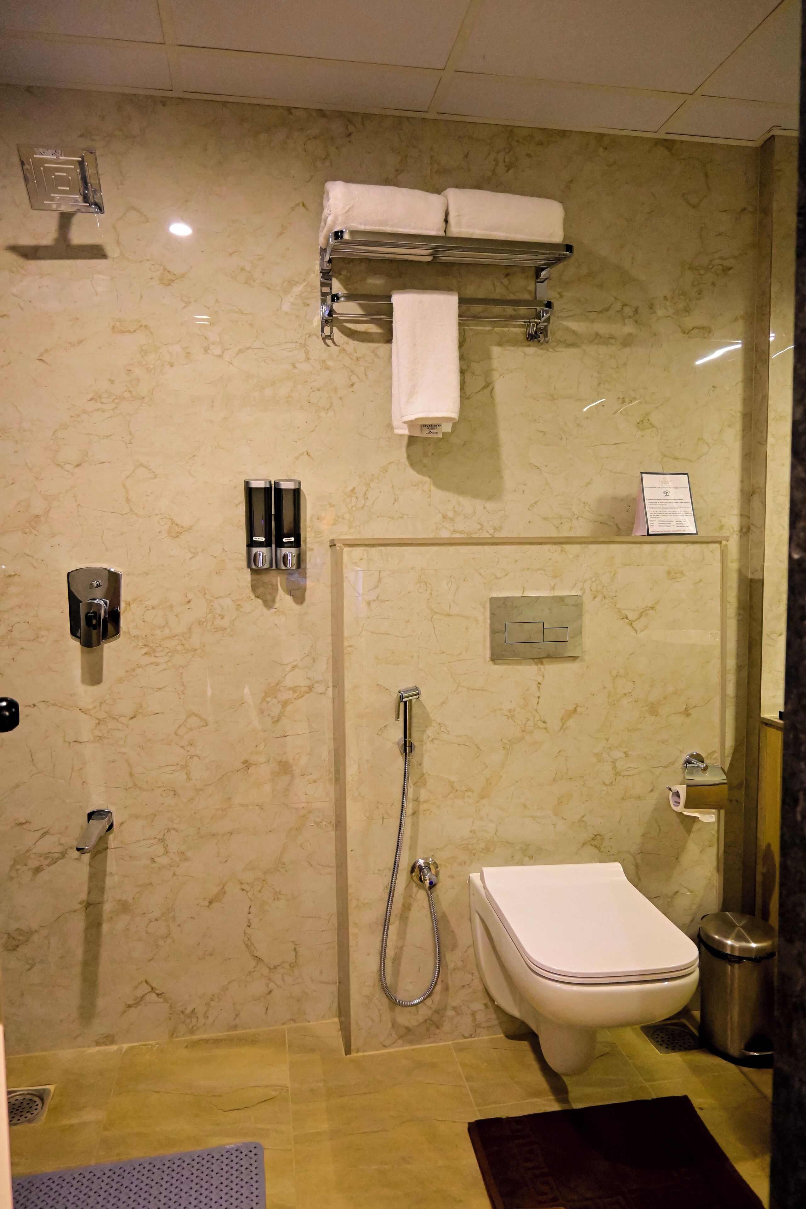 Un baño moderno con pared de mármol, ducha con cerramiento de vidrio, inodoro y toallero.