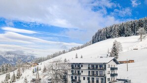 A modern multi-story hotel with a pool, surrounded by snow-covered trees and mountains. - Superior Apartment With Shared Pool (Sankt Martin am Tennengebirge)