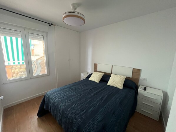 A bedroom with a bed, a nightstand, a wardrobe, and a window with a view of a building. - Apartment Los Narejos (Los Alcázares)