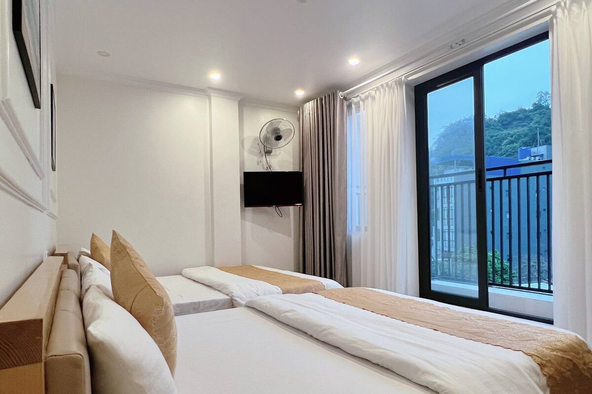 A hotel room with a bed, a TV mounted on the wall, and a window with a view of a balcony.