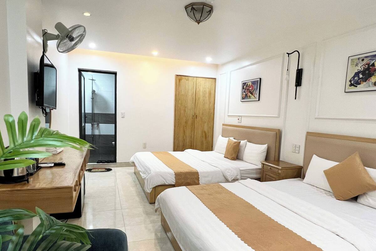 A hotel room with two beds, a desk with a plant, a TV, and a wooden wardrobe.
