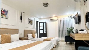 Quarto de hotel com duas camas, uma escrivaninha, uma cadeira, uma televisão e um ventilador.