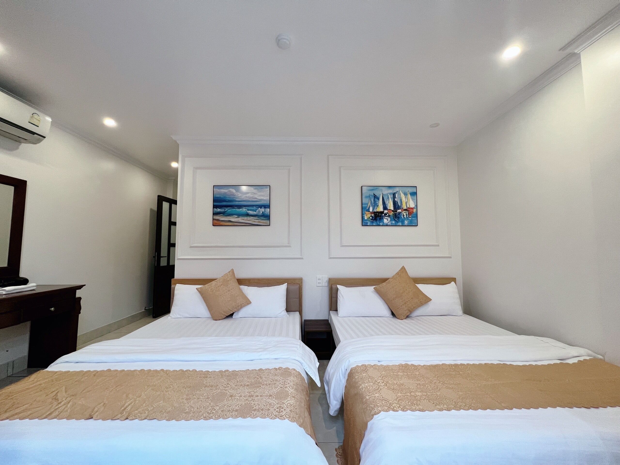 A hotel room with two beds, white bedding, beige throw pillows, and two framed artworks on the wall.