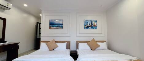 A hotel room with two beds, white bedding, beige throw pillows, and two framed artworks on the wall.
