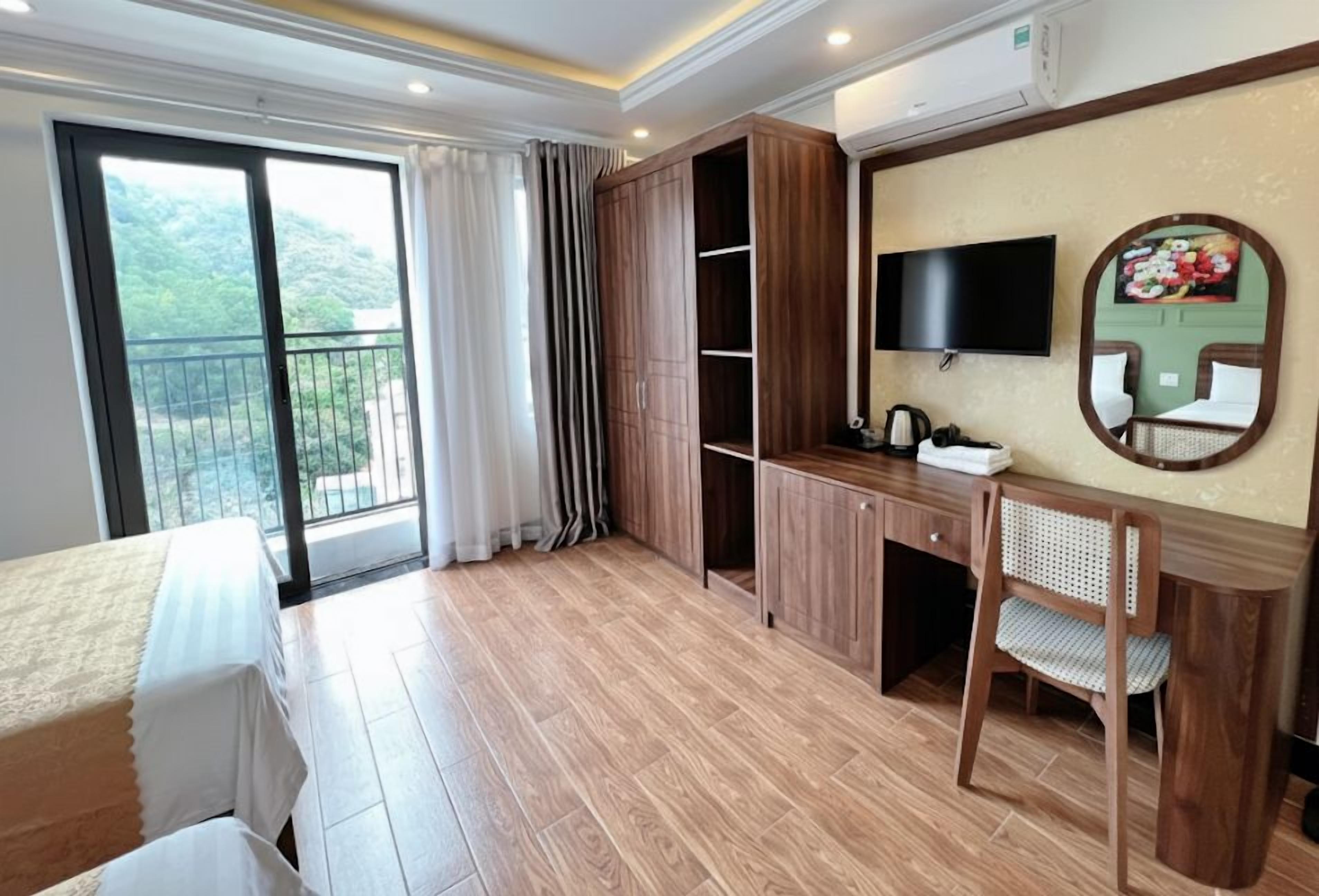 Une chambre d’hôtel équipée d’un lit, d’un bureau, d’une chaise, d’une télévision et d’une grande fenêtre donnant sur un paysage verdoyant.