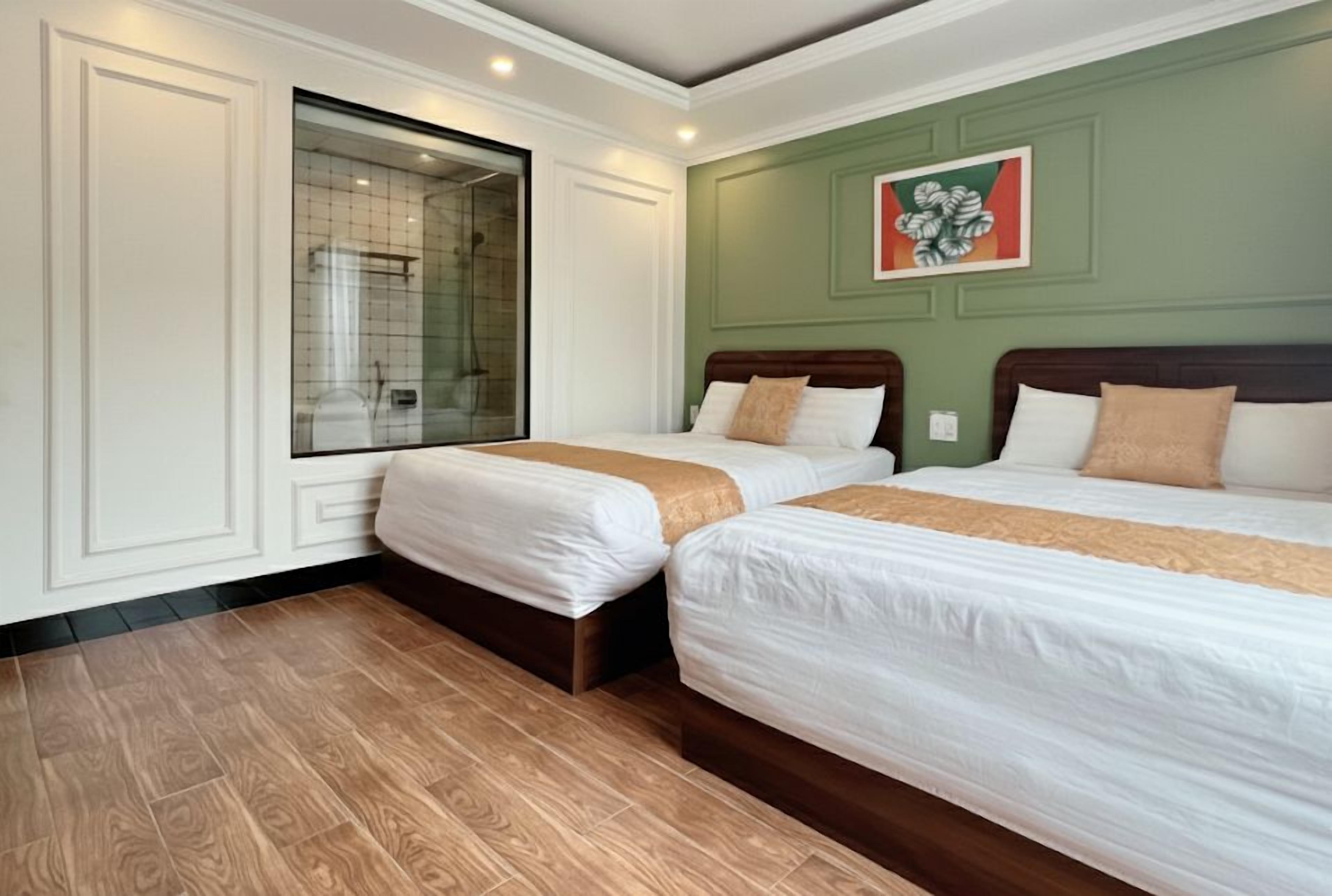 A hotel room with two beds, a large window, and a green wall with a floral painting.