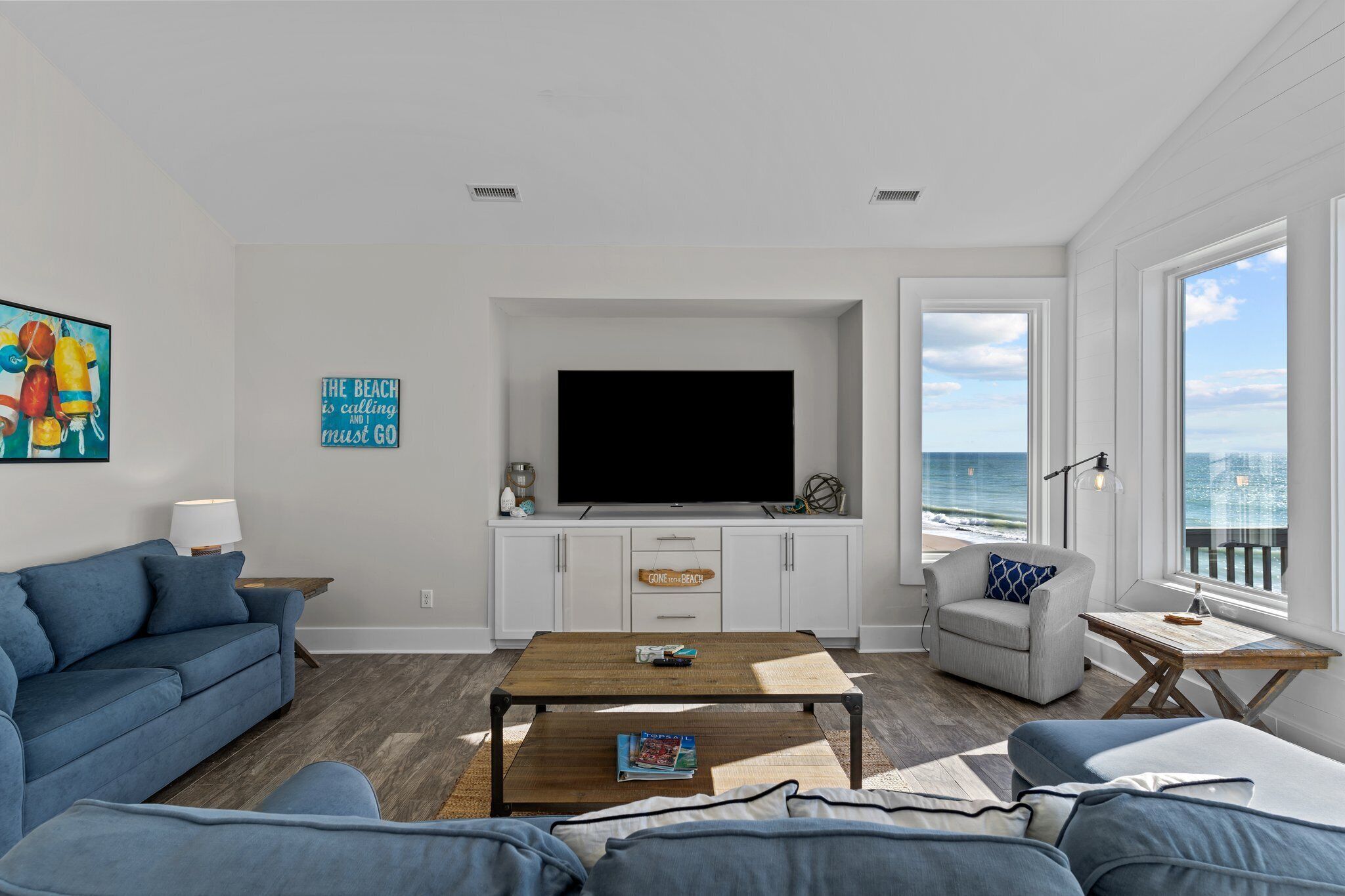 A modern living room with a large flat-screen TV, a sofa, a coffee table, and a view of the ocean.