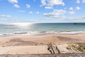 A beach with a wooden boardwalk leading to a pier extending into the ocean. - In Spiaggia (at the beach) #185 - 6 BD Oceanfront in the heart of Surf City! (Surf City)