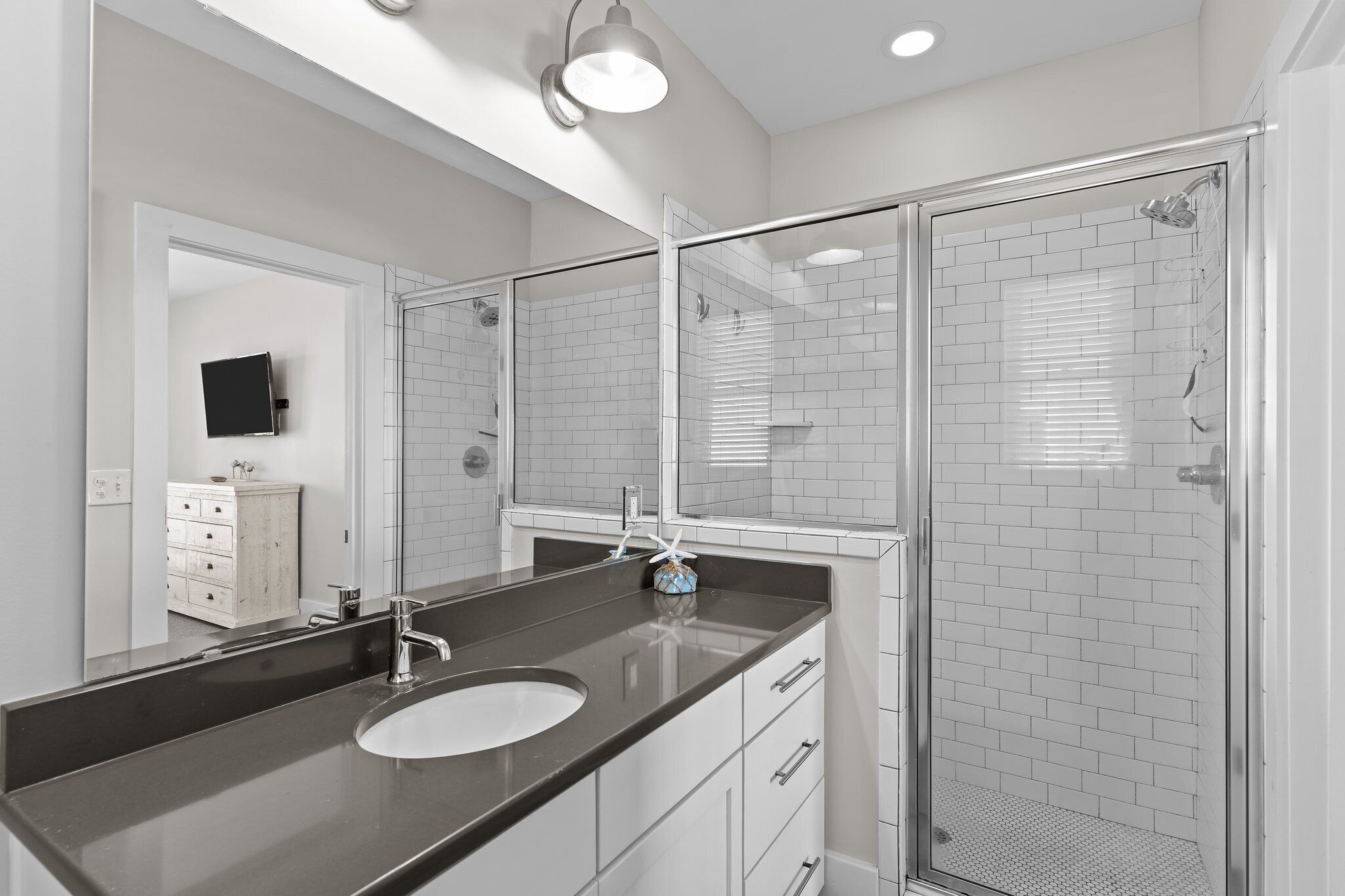 A modern bathroom with a glass-enclosed shower, a large mirror, and a dark countertop sink.