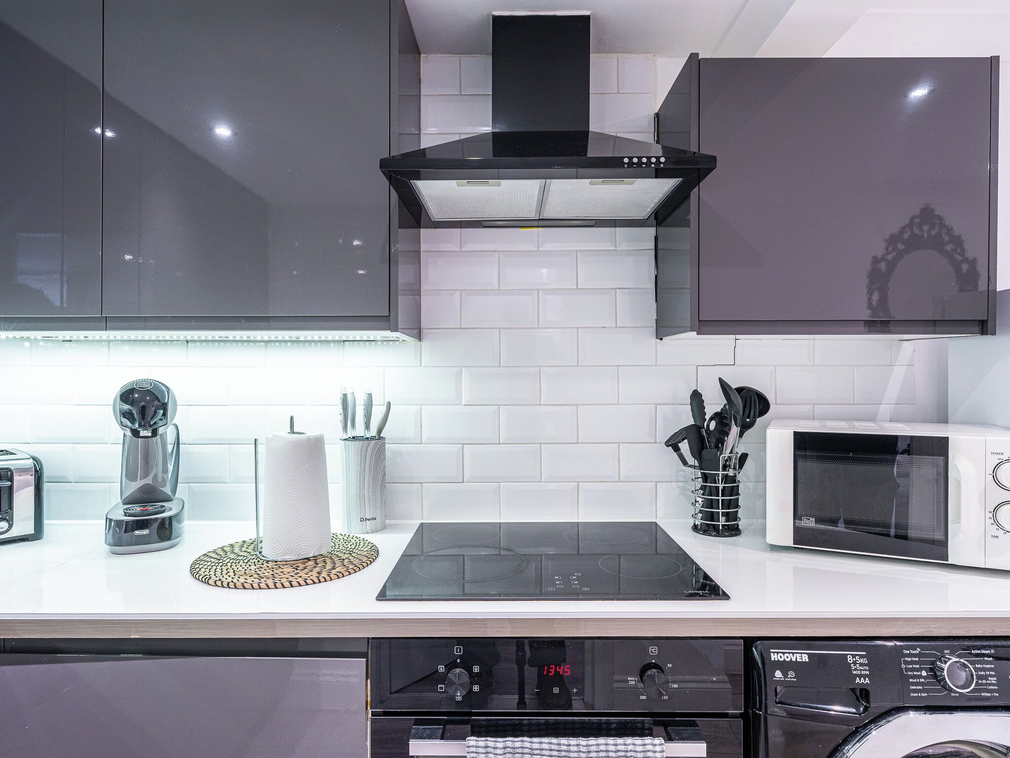 A modern kitchen with a built-in microwave, toaster, and a digital clock displaying 1345.