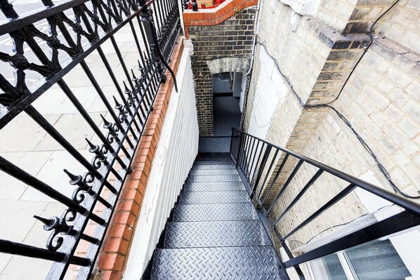 Stairs lead upwards through the building, featuring a non-slip metal surface and a brick wall with a window.