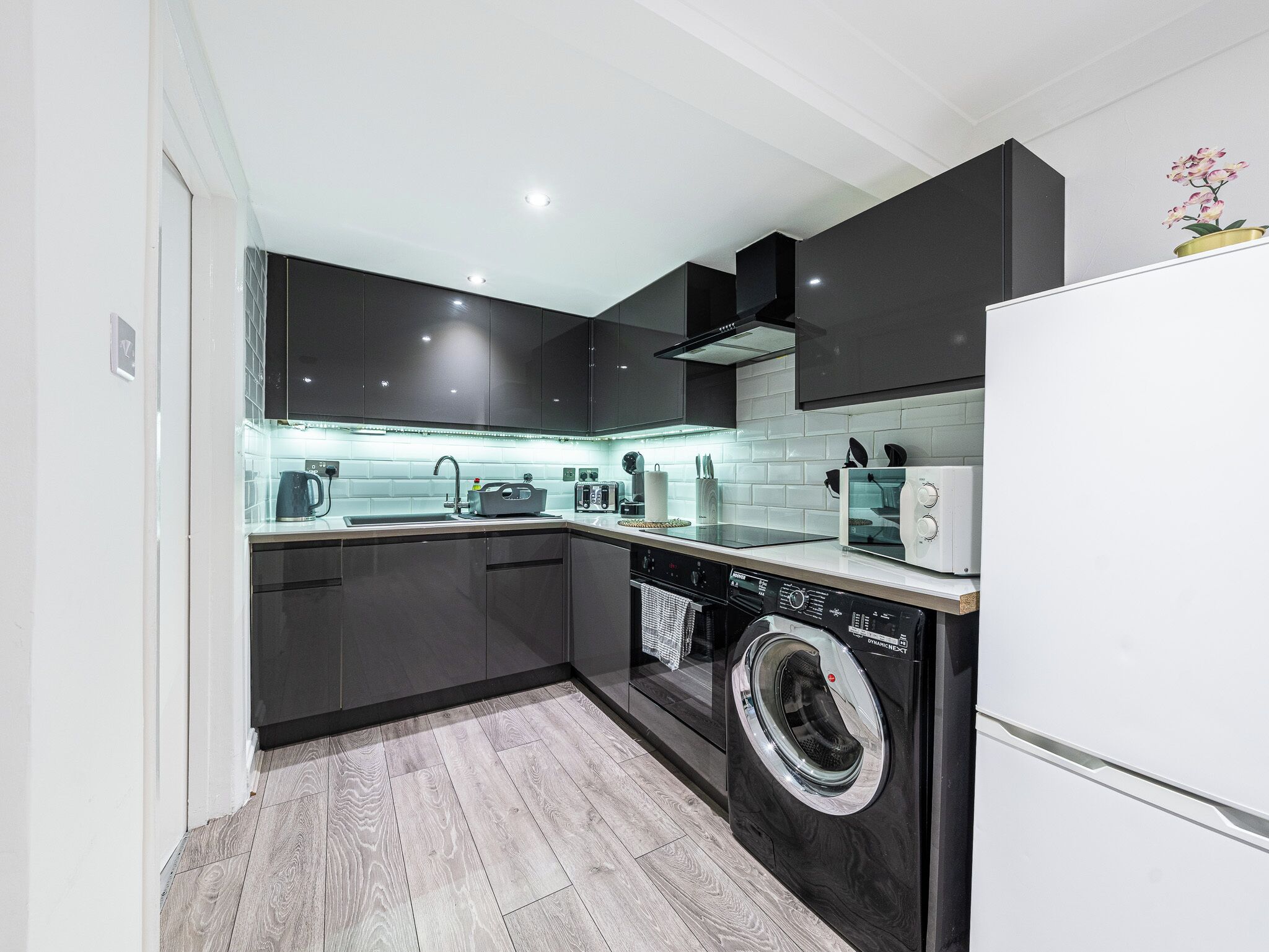 A modern kitchen with dark cabinetry, a built-in washing machine, and a white refrigerator.