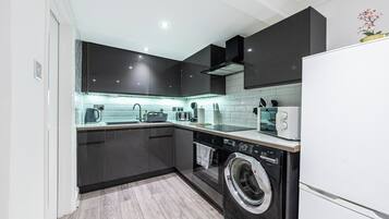 A modern kitchen with dark cabinetry, a built-in washing machine, and a white refrigerator.