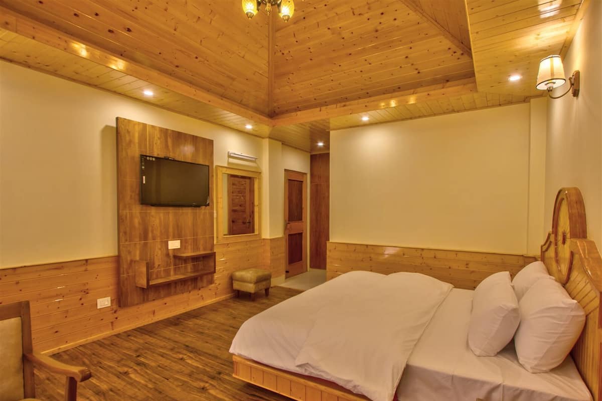 A wooden-paneled bedroom with a bed, a TV, a telephone, and a small stool.