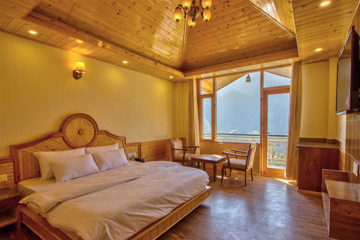 A wooden-paneled bedroom with a large bed, a desk, and a chair. There is a window with a view of the outside.