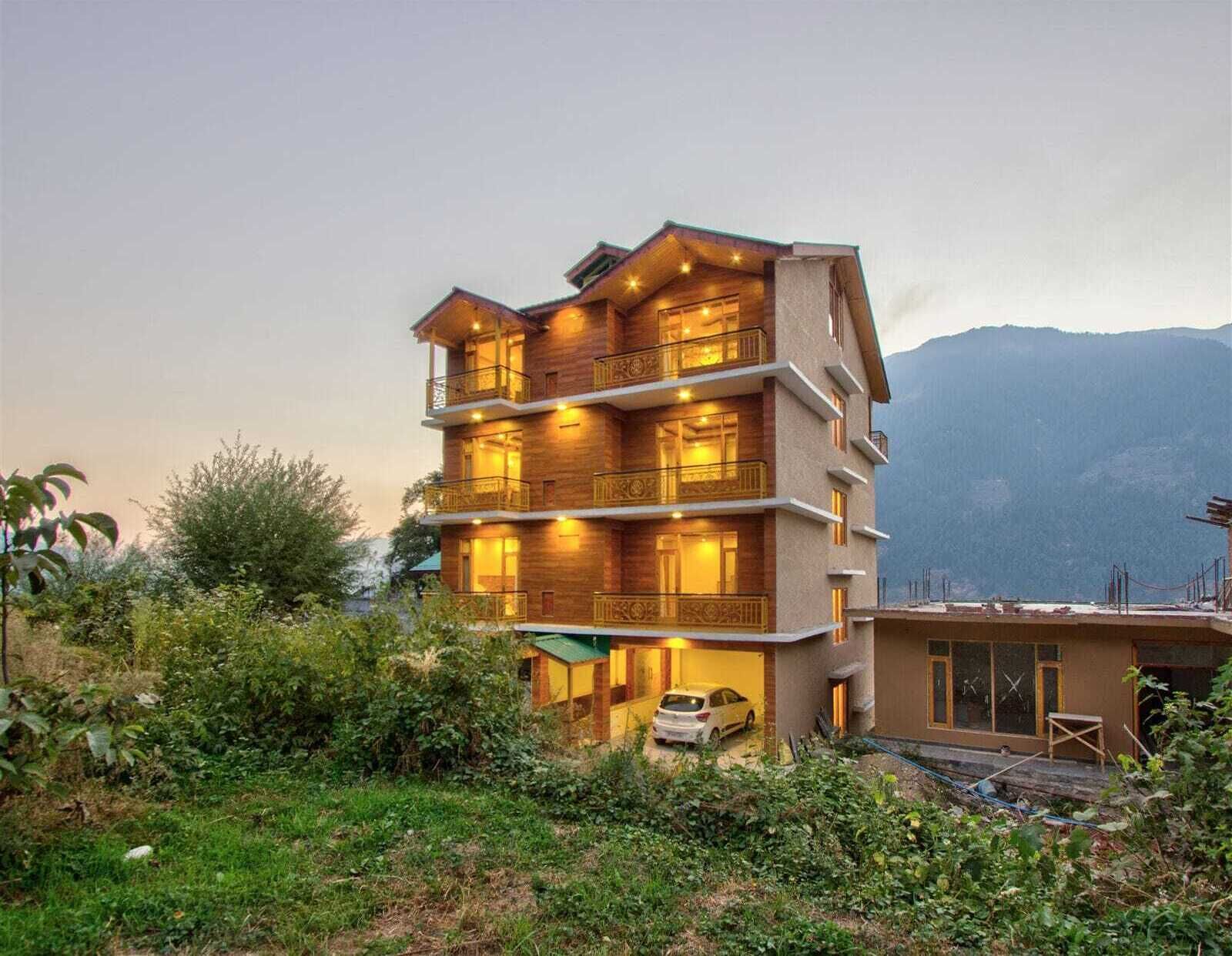 A multi-story hotel with balconies, a car parked in front, and a mountainous backdrop.