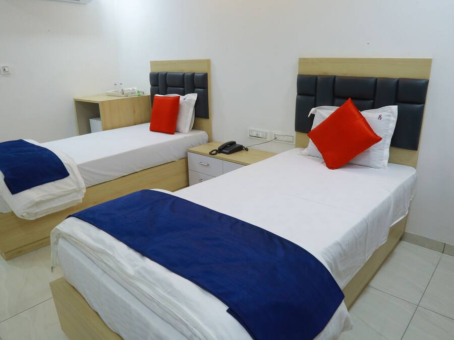 A hotel room with two single beds, each with a headboard, a bedside table, and a nightstand.