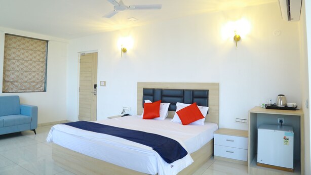 A hotel room with a bed, a desk, a chair, a ceiling fan, and a wall-mounted heater. - Anika Suites (Hyderabad)