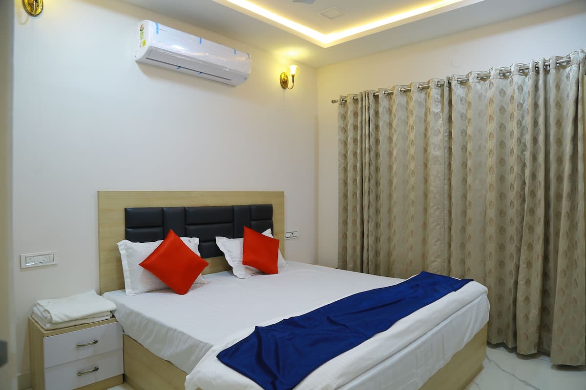 A hotel room with a bed, a nightstand, an air conditioning unit, and a curtain.