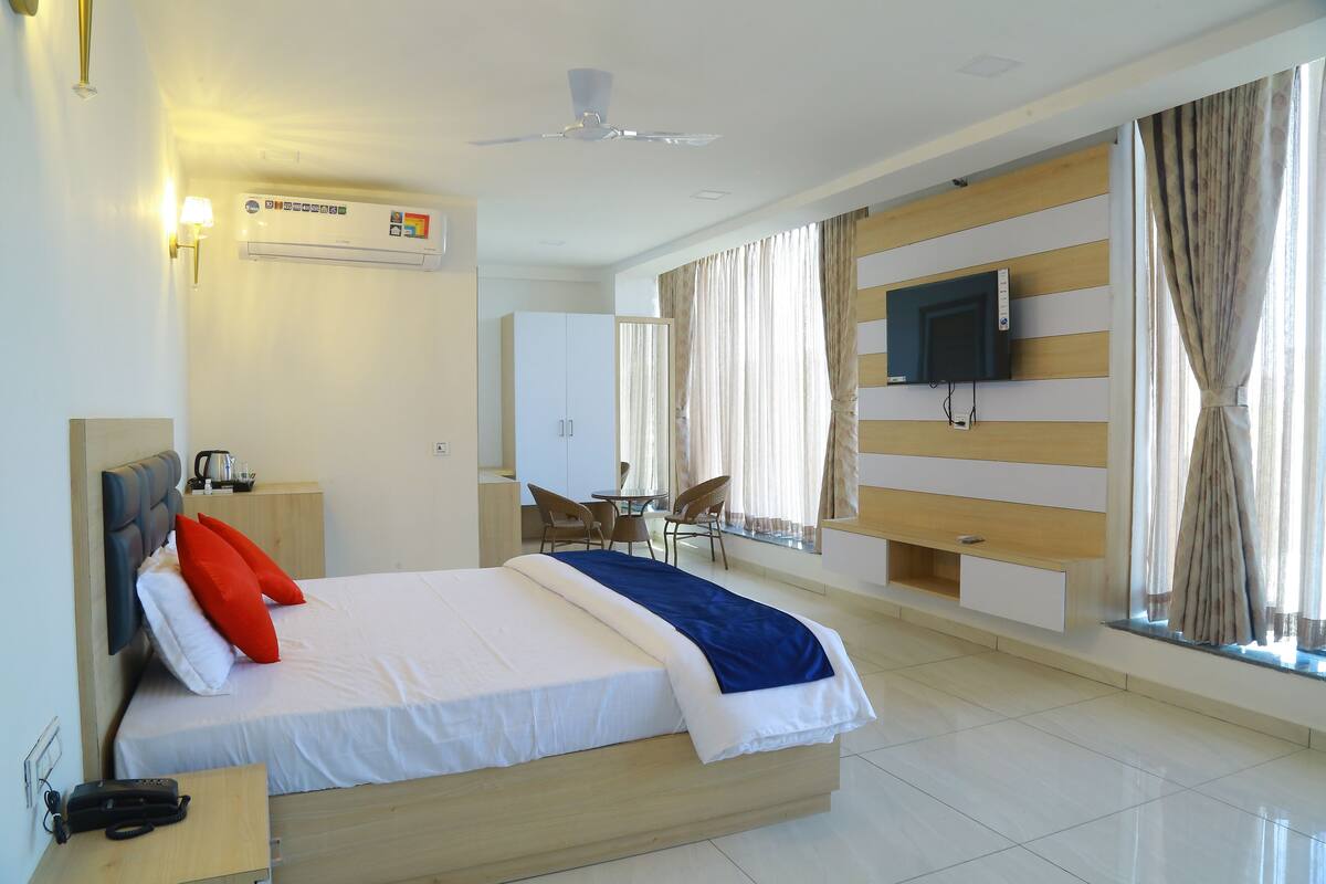 A hotel room with a bed, a desk, a chair, a TV, and a window with curtains.