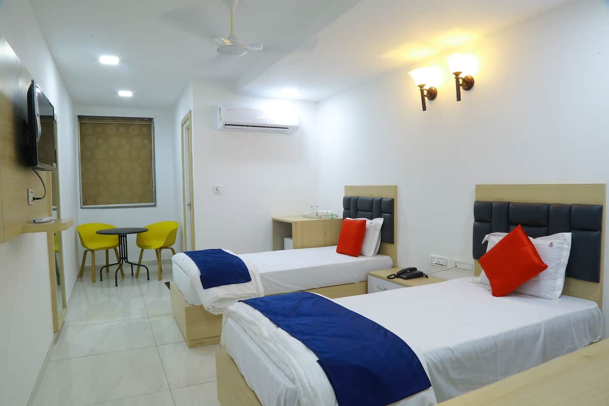 A hotel room with two single beds, a desk, a chair, and a TV mounted on the wall.