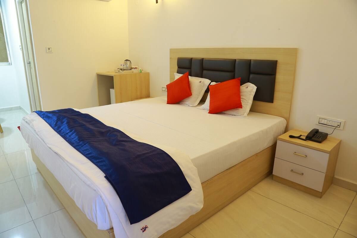 A neatly made bed with a blue blanket, two red pillows, and a wooden headboard.