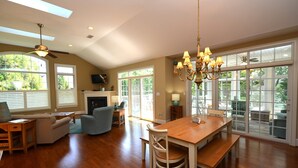A spacious living room with a wooden dining table, a ceiling fan, and large windows offering a view of the outdoors. - BEAUTIFUL HOME IN THE HIGHLY SOUGHT AFTER CANAL CORKRAN (Rehoboth Beach)