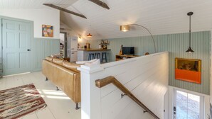 Un amplio salón con techo alto, una escalera de madera y una zona de cocina con taburetes.