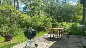 Un patio al aire libre con piso de piedra, una mesa redonda con sillas y una parrilla portátil.